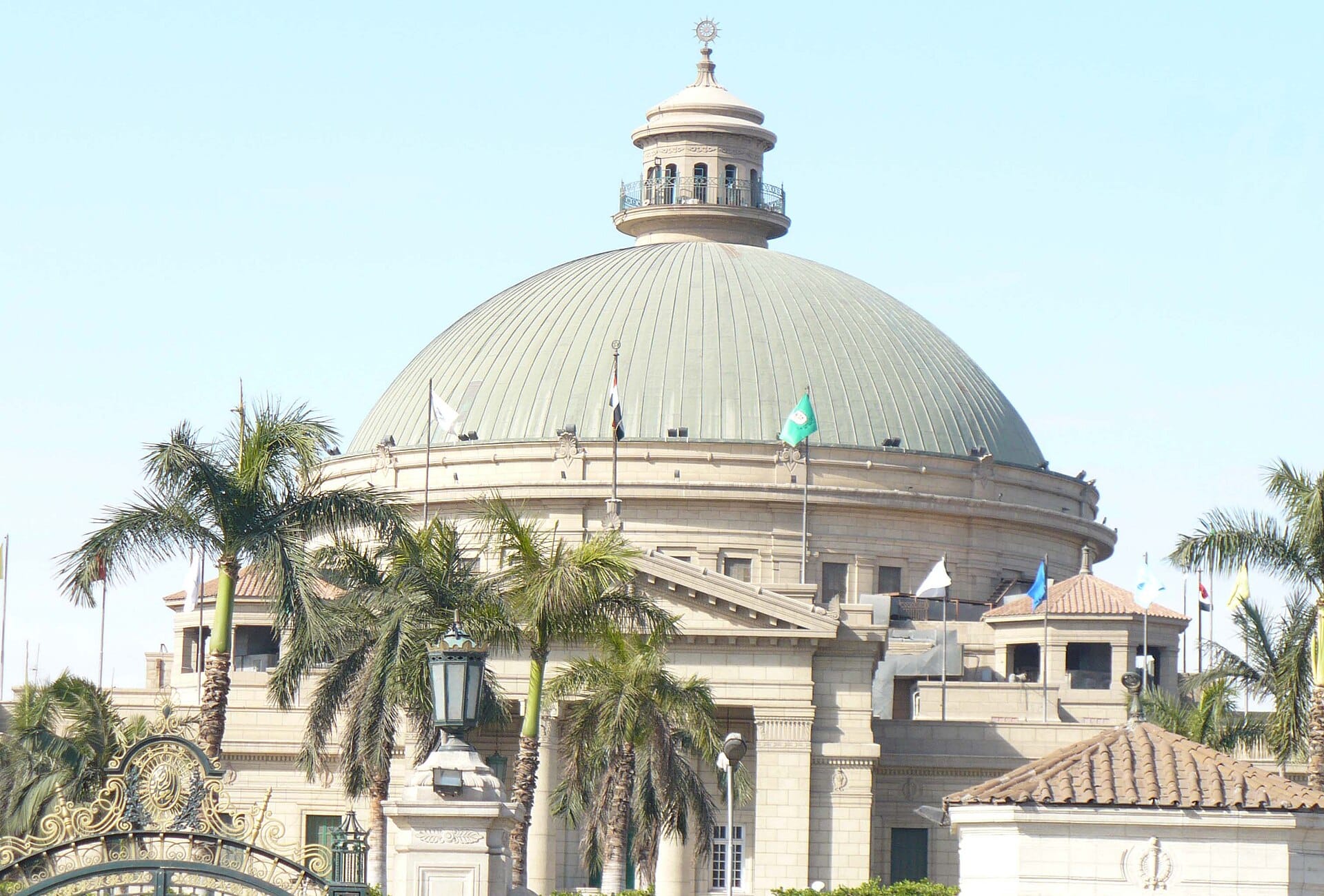 The green dome of the main building at Cairo University framed by palm trees