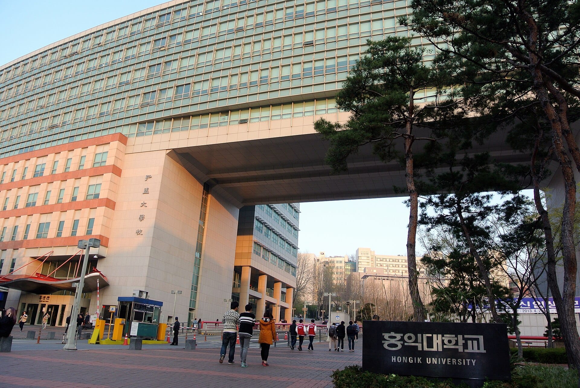 Students walking past the Hongik University sign beneath a large campus building